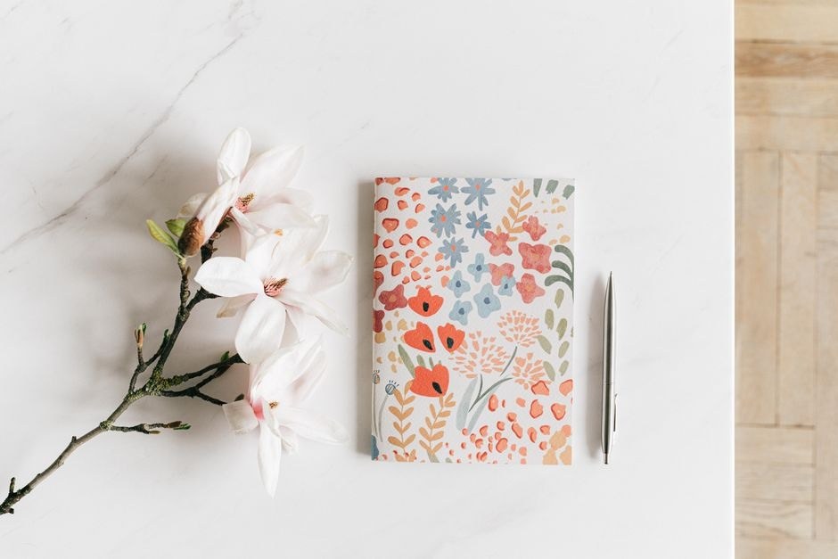 A floral notebook and pen arranged beside a flowering branch.